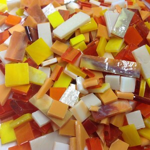 May include: A collection of small, colorful glass tiles in shades of yellow, orange, and white. The tiles are in various shapes and sizes, and they are perfect for mosaic projects.