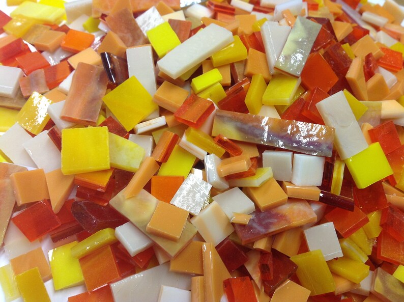 May include: A collection of small, colorful glass tiles in shades of yellow, orange, and white. The tiles are in various shapes and sizes, and they are perfect for mosaic projects.