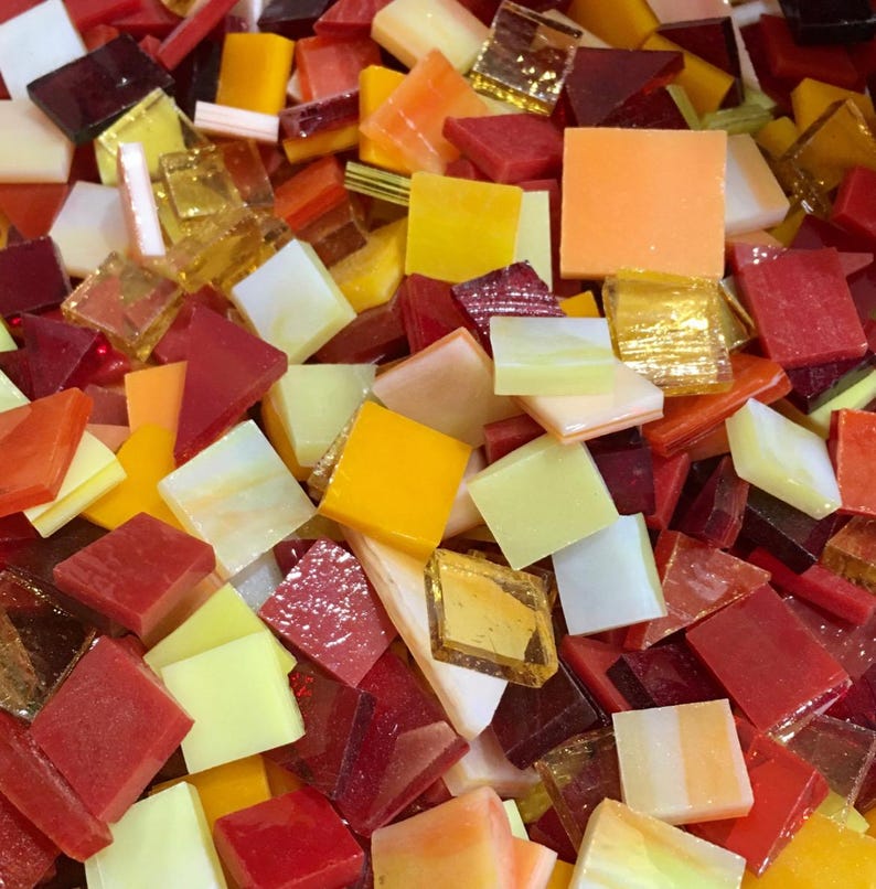 May include: A variety of small, square glass tiles in shades of red, orange, yellow, and white. The tiles are perfect for mosaic projects.