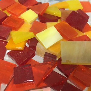 May include: A collection of small, square and rectangular glass tiles in shades of red, orange, and yellow. The tiles are translucent and have a glossy finish.