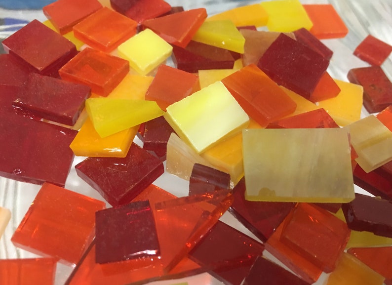 May include: A collection of small, square and rectangular glass tiles in shades of red, orange, and yellow. The tiles are translucent and have a glossy finish.