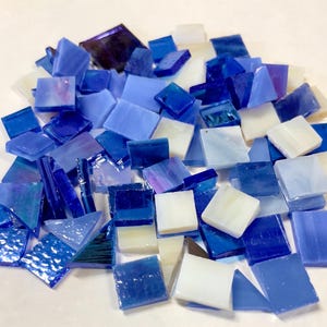 May include: A pile of blue and white glass mosaic tiles. The tiles are various shapes and sizes, with some having iridescent finishes.