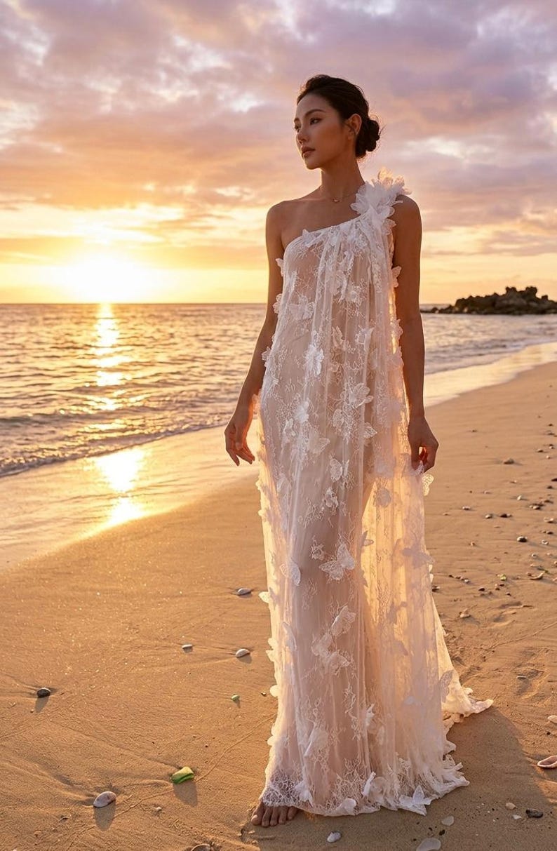 Puede incluir: Un vestido blanco de un solo hombro con aplicaciones de mariposas. El vestido se lleva en una playa al atardecer. El vestido tiene una silueta fluida y est&aacute; hecho de una tela transparente. La playa tiene arena dorada y el cielo est&aacute; lleno de colores c&aacute;lidos.