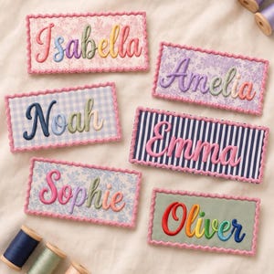 May include: Six rectangular fabric patches with scalloped edges, each featuring embroidered names: Isabella, Amelia, Noah, Emma, Sophie, and Oliver in various colours. The patches have different patterns including floral, gingham, and stripes, accompanied by six wooden spools of thread.