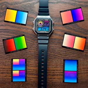 Könnte beinhalten: Eine schwarze digitale Casio-Uhr mit rechteckigem Zifferblatt und schwarzem Armband liegt mittig auf einer Holzoberfläche. Sechs kleine Karten mit farbenfrohen Farbverläufen und dem Text "CASIO FILTERS BY KLOKK.ETSY.SHOP" umgeben die Uhr.