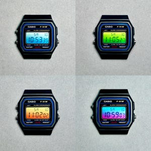 Op de afbeelding: Vier Casio F-91W digitale horloges met zwarte behuizingen en blauwe accenten. Elk horloge toont een andere tijd op het digitale scherm: 10:53:39, 11:05:27, 11:02:02 en 10:59:03. De horloges zijn waterbestendig.