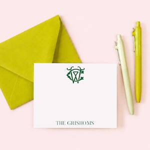 May include: A white rectangular note card featuring a dark green monogram logo at the top and the text THE GRISHOMS printed in dark green at the bottom, accompanied by a lime green envelope and two matching lime green ballpoint pens.