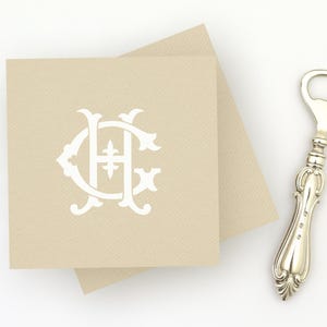 May include: A pair of square, light tan cards with a white monogram and a silver bottle opener. The monogram features the letters "C" and "H" intertwined. The bottle opener has a decorative handle.