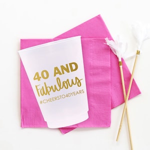 K&ouml;nnte beinhalten: Ein wei&szlig;er Plastikbecher mit goldener Aufschrift "40 AND Fabulous #CHEERSTO40YEARS". Der Becher liegt auf zwei rosa Servietten.