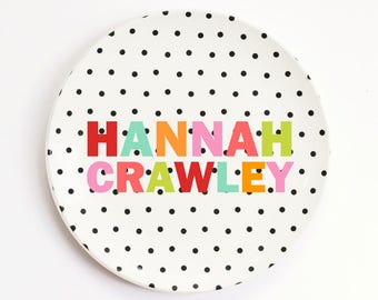 May include: A white ceramic plate with black polka dots and the name "HANNAH CRAWLEY" written in colorful letters.