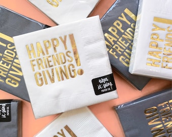 May include: White and gray paper napkins with gold foil lettering that reads "HAPPY FRIENDS GIVING." The napkins are packaged in clear plastic. A black sticker with white text reads "when it rains PAPER CO."