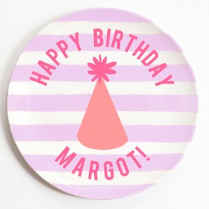 K&ouml;nnte beinhalten: Ein runder Teller mit rosa und wei&szlig;en Streifen mit dem Text "Happy Birthday Margot!" in rosa Schrift. In der Mitte des Tellers befindet sich eine rosa Partym&uuml;tze mit einem wei&szlig;en Bommel.