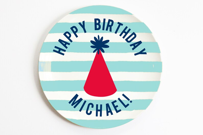K&ouml;nnte beinhalten: Ein blauer und wei&szlig; gestreifter Pappteller mit dem Text "Happy Birthday Michael!" in dunkelblauer Schrift. In der Mitte des Tellers befindet sich eine rote Partym&uuml;tze mit einem blauen Bommel.