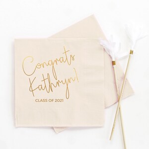 May include: Pink paper napkins with gold foil lettering that reads "Congrats Kathryn! Class of 2021".