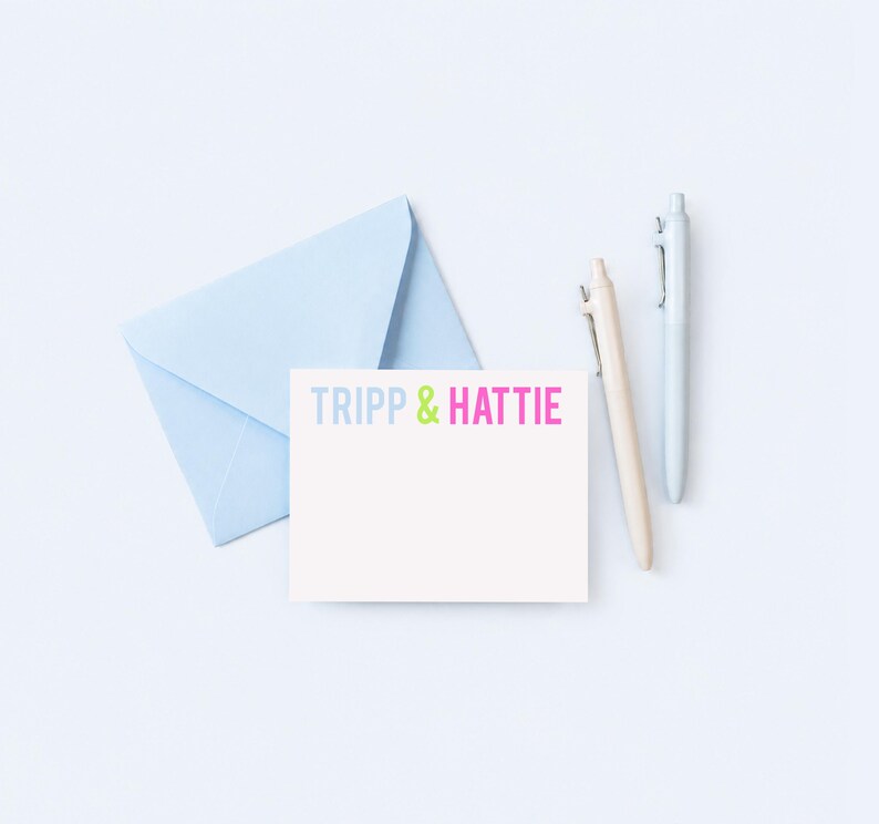 a light blue envelope, a blank white card with the text "TRIPP & HATTY" written on it, and two pens.