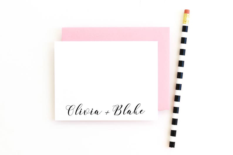 May include: A white card with the text "Olivia + Blake" written in black cursive script. The card is on top of a pink card.