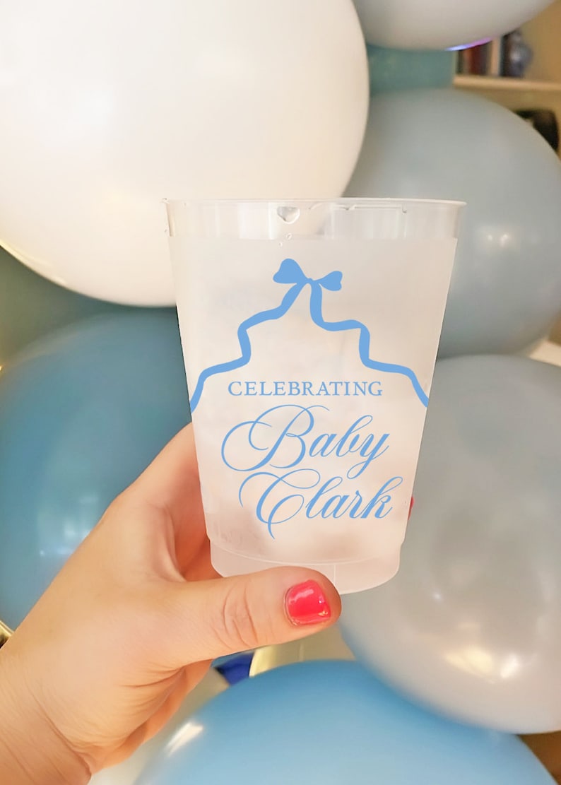 May include: A clear plastic cup with a blue ribbon design and the text "Celebrating Baby Clark" printed on it.