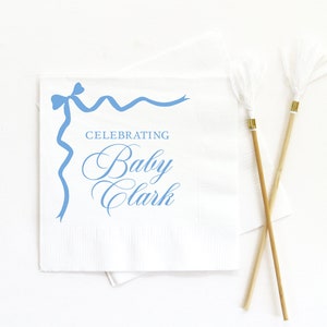 May include: White paper napkin with a blue ribbon design and the text "Celebrating Baby Clark".