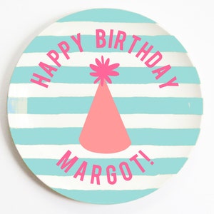 K&ouml;nnte beinhalten: Ein blauer und wei&szlig; gestreifter Pappteller mit dem Text "Happy Birthday Margot!" in rosa Schrift. Ein rosa Partyhut mit einem wei&szlig;en Bommel befindet sich in der Mitte des Tellers.