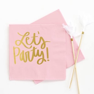 Op de afbeelding: Roze papieren servetten met gouden letters die "Let's Party!" zeggen