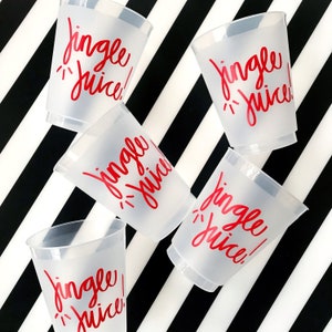 May include: A collection of frosted plastic cups with the words "Jingle Juice!" in red script. The cups are scattered on a black and white striped background, creating a festive and playful arrangement.