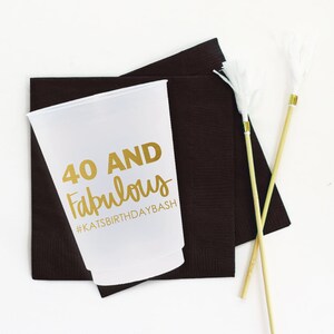 K&ouml;nnte beinhalten: Ein wei&szlig;er Plastikbecher mit goldener Aufschrift "40 AND Fabulous #KATSBIRTHDAYBASH". Der Becher steht auf zwei schwarzen Servietten.