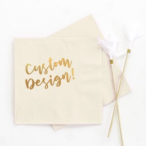 May include: A beige paper napkin with the words "custom design!" printed in gold foil.