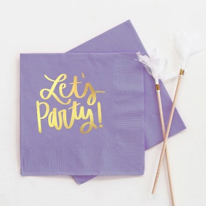 Op de afbeelding: Paarse papieren servetten met gouden letters die "Let's Party!" zeggen