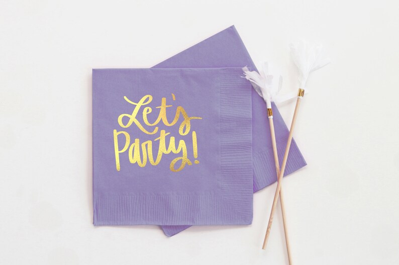 Op de afbeelding: Paarse papieren servetten met gouden letters die "Let's Party!" zeggen
