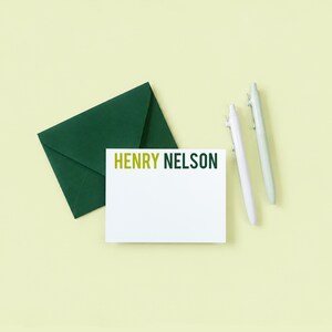 a green envelope, a blank white card with the name "HENRY NELSON" written on it, and two pens.