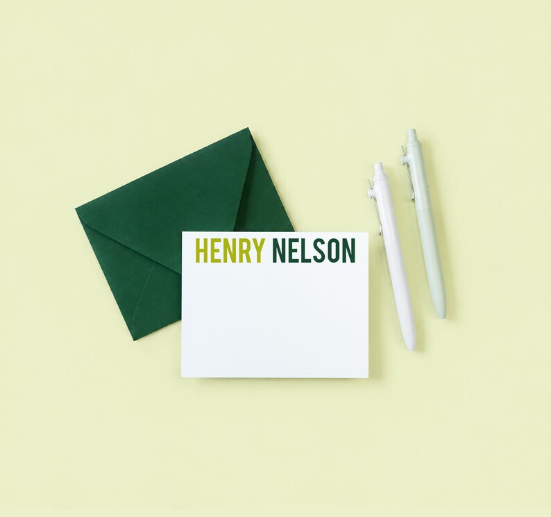 a green envelope, a blank white card with the name "HENRY NELSON" written on it, and two pens.