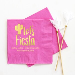 May include: Pink paper napkins with gold foil lettering that says "Let's Fiesta" with a cactus graphic. The text below reads "Katey Miller - GHS Graduate #TacoBoutGrad"