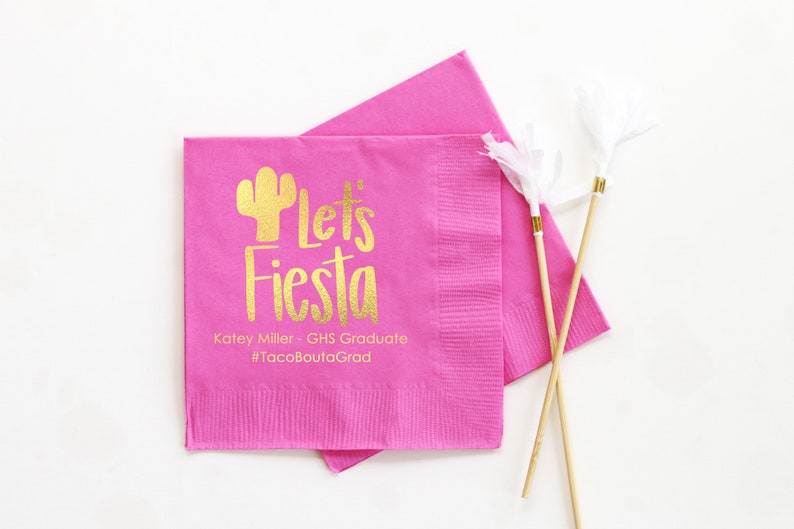 May include: Pink paper napkins with gold foil lettering that says "Let's Fiesta" with a cactus graphic. The text below reads "Katey Miller - GHS Graduate #TacoBoutGrad"