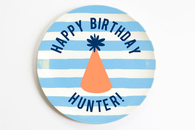 K&ouml;nnte beinhalten: Ein blauer und wei&szlig; gestreifter Keramikteller mit dem Text "Happy Birthday Hunter!" in dunkelblauer Schrift. In der Mitte des Tellers befindet sich eine Partym&uuml;tze mit einem blauen Bommel.