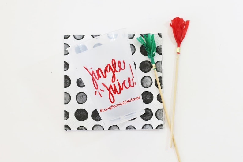 May include: A clear plastic cup with the words "Jingle Juice!" in red, resting on a square napkin with black and gray polka dots. Two decorative wands with red and green accents are also present.