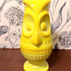 May include: A bright yellow owl-shaped decorative container. The container has large, round eyes, a prominent beak, and a textured surface. It is a vintage-style piece, likely made of glass or ceramic, and sits on a round base.