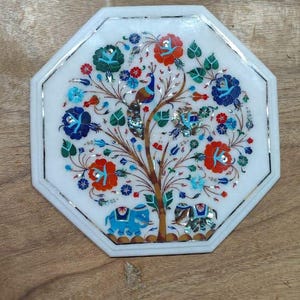 Puede incluir: Bandeja decorativa octogonal de mármol blanco con un diseño de árbol incrustado. El árbol presenta flores rojas, azules y verdes, un pavo real y elefantes. La bandeja tiene un borde plateado.