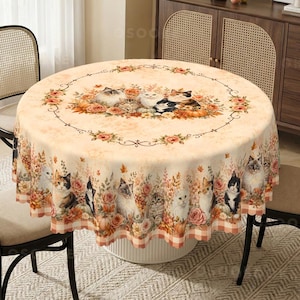 May include: A round tablecloth featuring a cream-colored background with a repeating pattern of various cats, orange pumpkins, and autumn-toned flowers. The design includes a central circular floral border and a scalloped edge with a checkered trim.