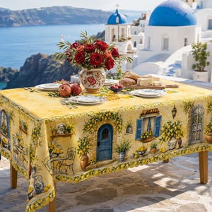 Peut inclure: Une nappe rectangulaire jaune ornée d'un motif imprimé représentant des bâtiments en pierre de style méditerranéen, des portes bleues et des citronniers. Le tissu présente un bord festonné et recouvre une table avec un vase de roses rouges.