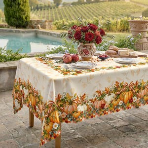 May include: A rectangular tablecloth featuring a cream-coloured base with a vibrant border print of orange pumpkins, autumn leaves, and white flowers. The centre of the table displays a ceramic vase filled with deep red roses and pomegranates.