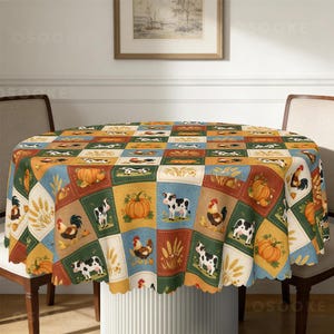 May include: A round tablecloth featuring a grid pattern of squares with illustrations of black and white cows, roosters, orange pumpkins, and stalks of wheat. The squares are coloured in shades of blue, green, orange, and cream, creating a farm theme.