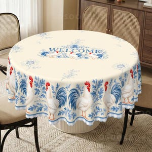 May include: A round tablecloth with a cream-colored background featuring a repeating pattern of white roosters with red combs and blue tail feathers, blue floral accents, and the word WELCOME printed in blue text on the top surface.
