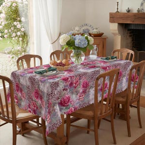 May include: A rectangular tablecloth with a floral and leopard print design. The tablecloth features pink roses and a gray leopard print border. The table is set with plates, napkins, and a vase of flowers. The table is surrounded by wooden chairs.