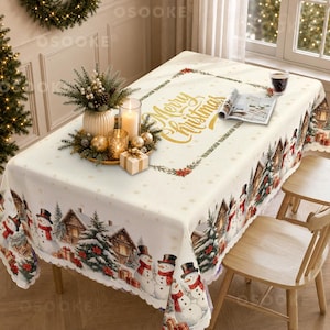 Könnte beinhalten: Eine rechteckige Tischdecke mit cremefarbenem Hintergrund und goldenem Merry Christmas Schriftzug in der Mitte. Der Rand zeigt eine winterliche Szene mit Schneemännern, Tannen und Hütten. Ein Tischgesteck mit Kerzen und Grün steht darauf.