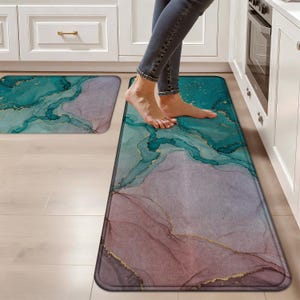 May include: Two rectangular kitchen floor mats featuring an abstract marble-like pattern in shades of teal, lavender, and soft pink, accented with thin, shimmering gold-toned veins throughout the design, providing a soft surface for standing.