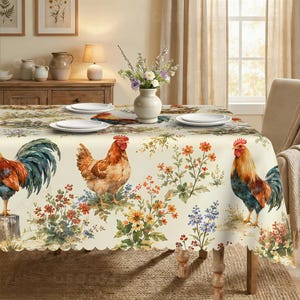 May include: A cream-colored tablecloth featuring a repeating pattern of roosters, hens, and colorful wildflowers. The fabric has a scalloped edge and is set with white plates and a central white vase filled with a bouquet of flowers.