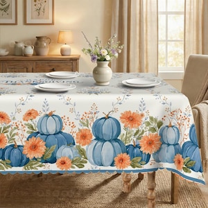 May include: A rectangular tablecloth featuring a white background with a repeating pattern of light blue pumpkins and orange flowers. The text "HAPPY THANKSGIVING" is printed in blue on the top surface. The edges have a scalloped blue trim.