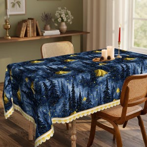 May include: A rectangular blue tablecloth with a forest and camping tent design. The pattern features yellow tents, trees, and stars. The tablecloth has a yellow and white scalloped edge. The tablecloth is on a wooden table with two wicker chairs.