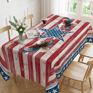 May include: A rectangular tablecloth featuring a distressed American flag pattern with red and white vertical stripes, a large central blue star, and two bald eagles in flight. The edges are decorated with a blue border containing white stars.