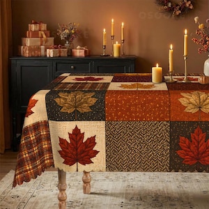 May include: A rectangular tablecloth featuring a patchwork design of autumn maple leaves in shades of red, orange, and brown, interspersed with plaid and textured patterns. The fabric has a scalloped edge and covers a table in a warm-toned room.